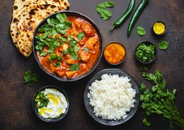 Plato de Butter Chicken con arroz basmati, naan y chutneys, sobre un fondo oscuro