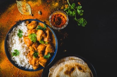 Bowl de Butter Chicken servido con arroz y naan, acompañado de especias