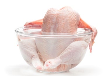 Carcasa de pollo cruda sumergida en un bowl de agua transparente, lista para cocinar un caldo de hueso de pollo casero