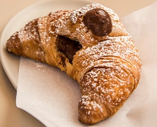 Delicioso croissant relleno de chocolate y espolvoreado con azúcar pastelera, similar al croissant de almendras.