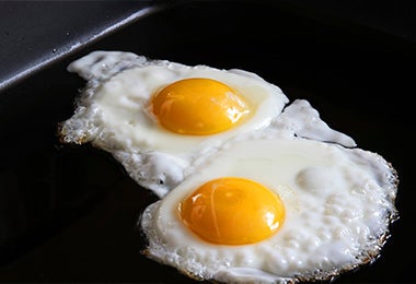 Dos huevos fritos en una parrilla con una superficie negra para preparar huevos shakshuka