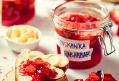 Mermelada de ruibarbo y fresas servida sobre tostadas con frascos en el fondo