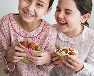 Niñas degustando alegremente pitas rellenas de falafel, un pan árabe