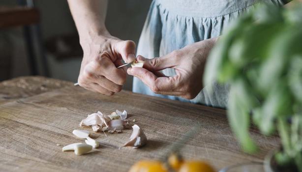 Mujer pelando ajos con cuchillo, qué hacer al cortarse en la cocina