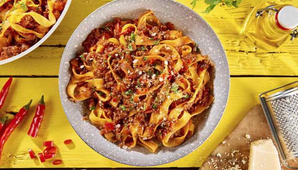 Pasta a la boloñesa con carne, queso parmesano y hierbas aromáticas sobre un fondo amarillo.  